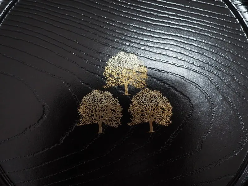 黑色盘面局部近景，可见弧形纹理和三棵金色树形装饰